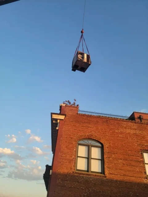 a crane lifting a box on a brick building Commercial HVAC Services